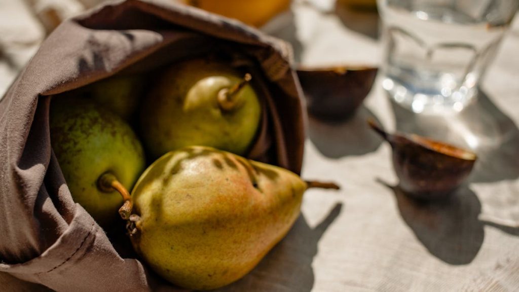 A cozy arrangement of fresh pears in a cloth bag, casting natural shadows on a sunlit table.